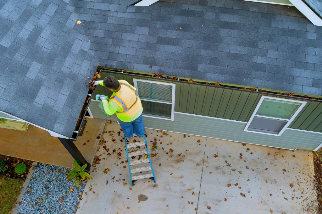 Roof cleaning involves a worker removing leaves from gutters using a ladder