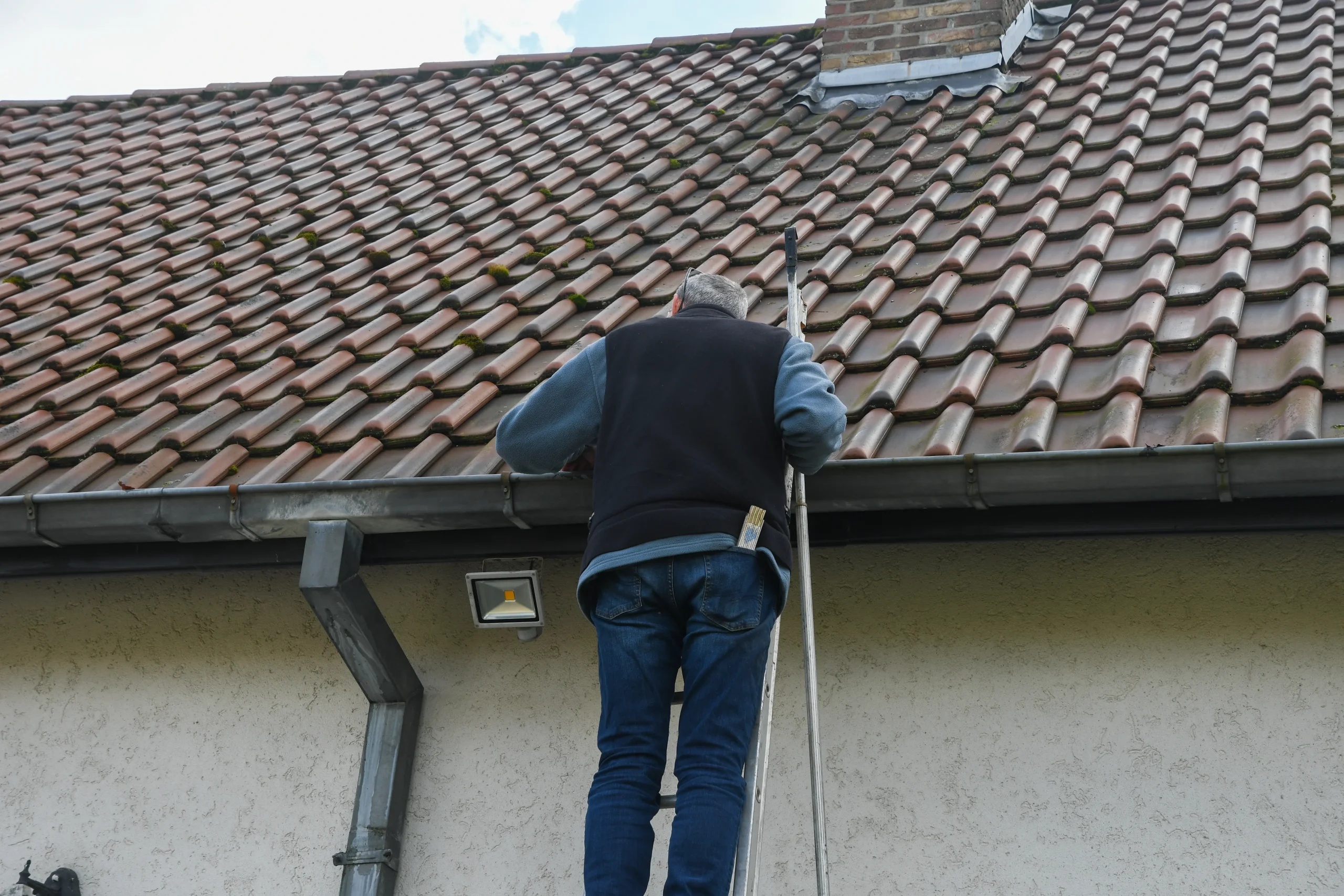 Gutter cleaning process with a person inspecting a roof using a long tool