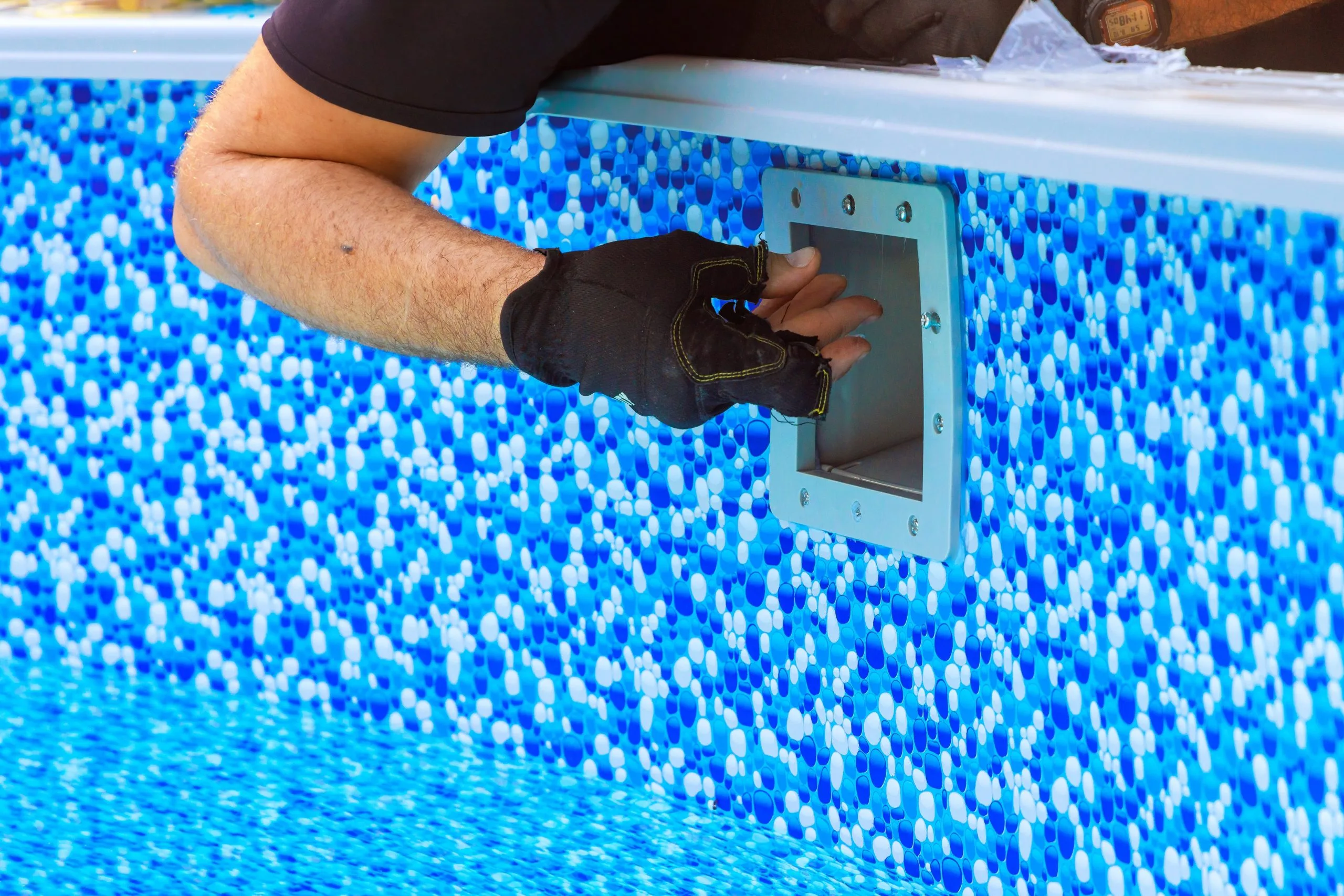 Pool service technician installing a fixture in a vibrant blue tiled pool wall