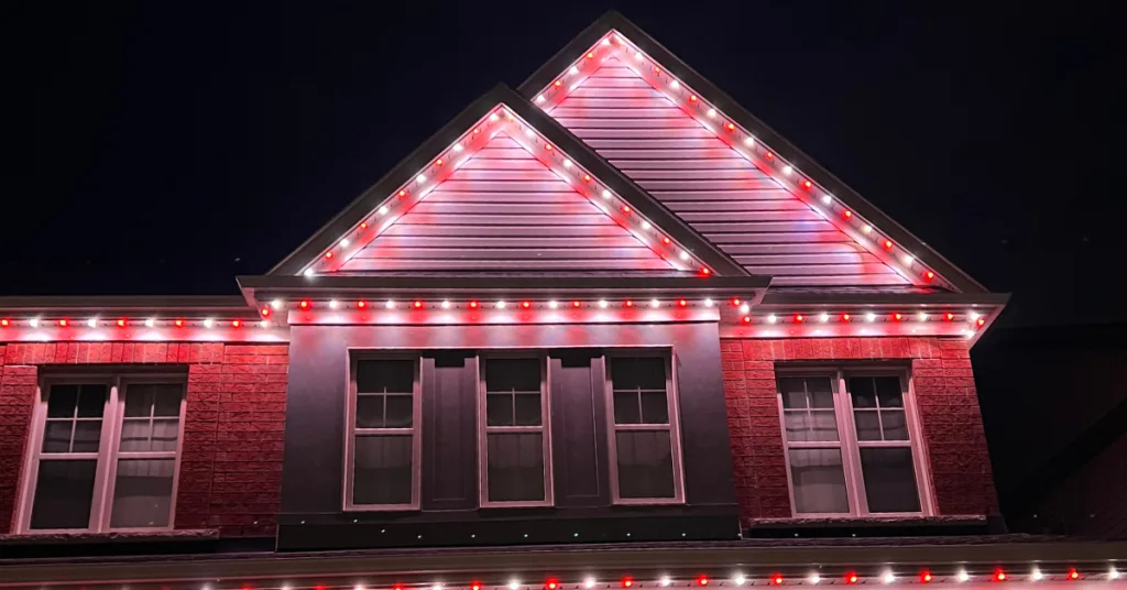 Bright red and white lights illuminate the triangular roof of a house at night