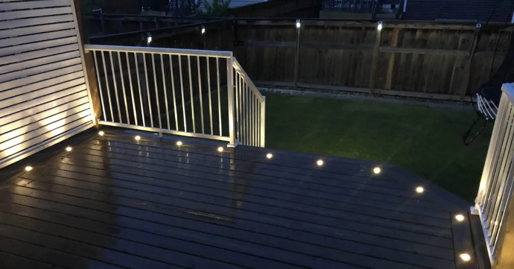 A wooden deck illuminated by soft lights, leading to a grassy backyard