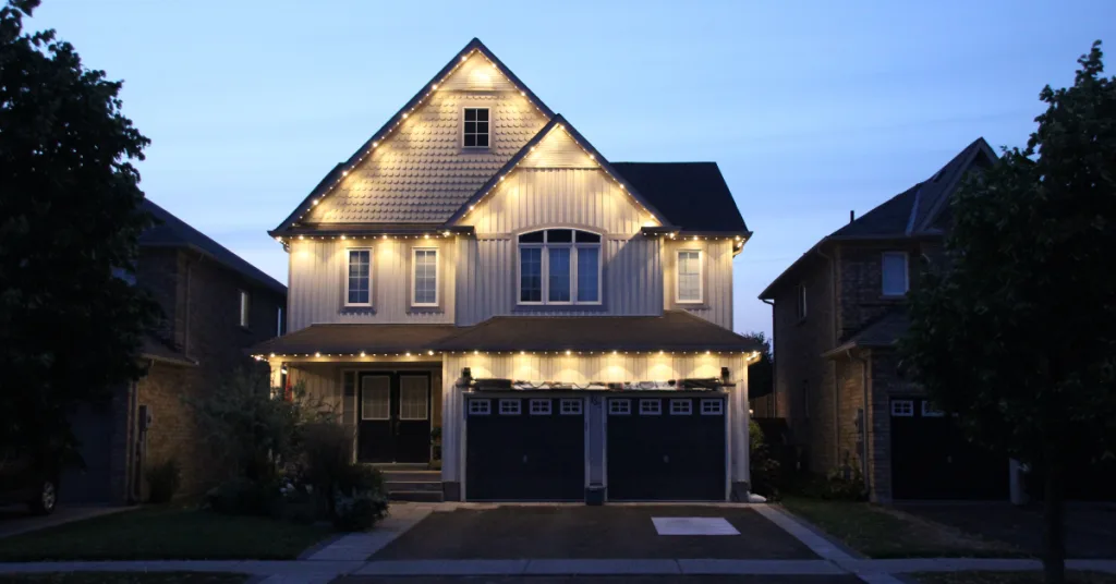 A cheerful house is adorned with warm string lights, glowing against the evening dusk